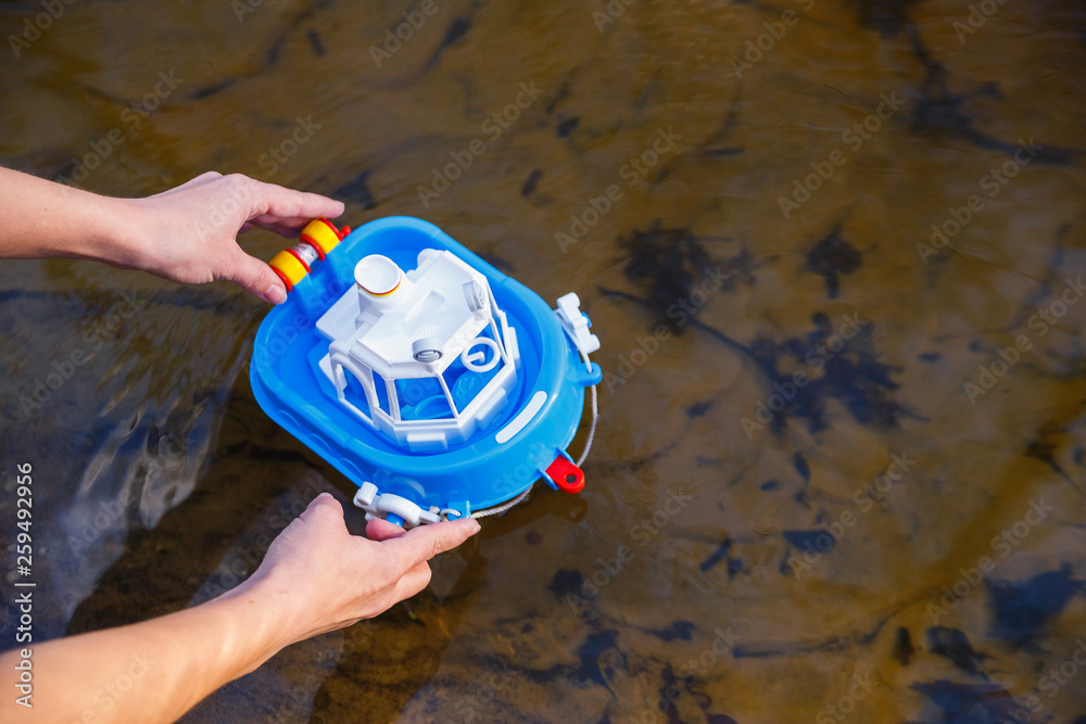 Girl puts his self-made toy boat into river in forest stock photo