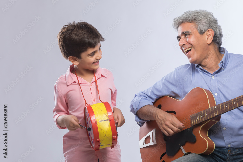 Grandfather playing guitar and grandson beating drum	