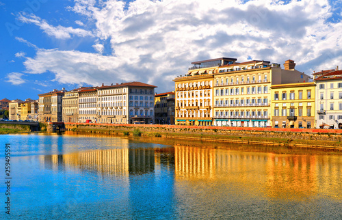 waterfront and riverscape with colorful reflections and old historical buildings and brigde on Arno river and cloudy blue sky in background in old part of Florence