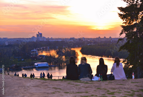 four young girls on Kalemegdan fortress park hill looking warm colorful sunset on Danube river  with horizon of New Belgrade in background in Belgrade, Serbia