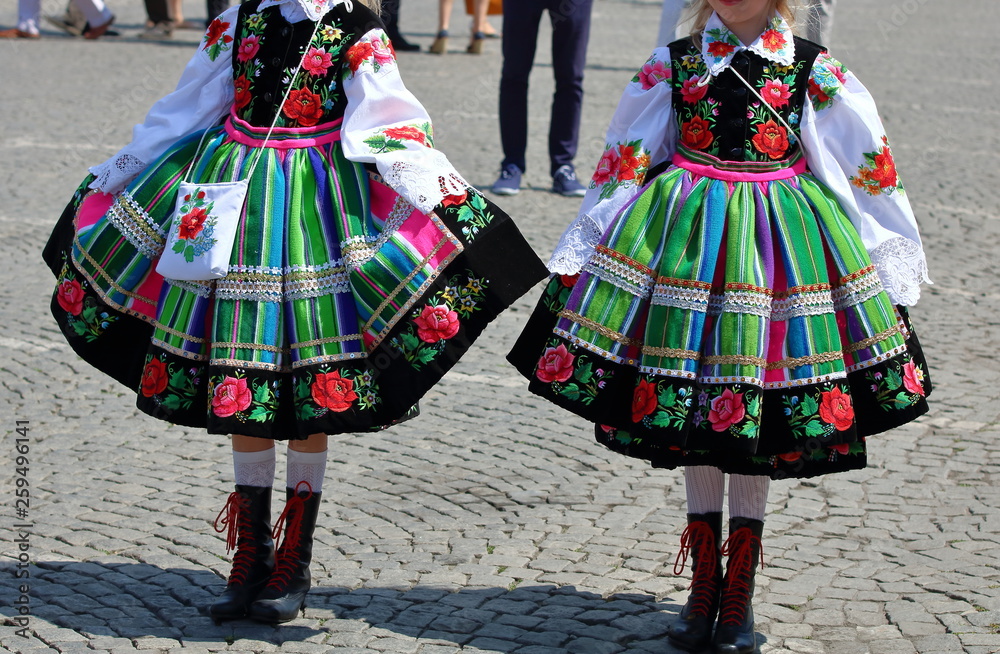 two girls dressed in traditional regional folk costumes from Lowicz region,  Poland, on square, show colorful striped skirts, Stock Photo