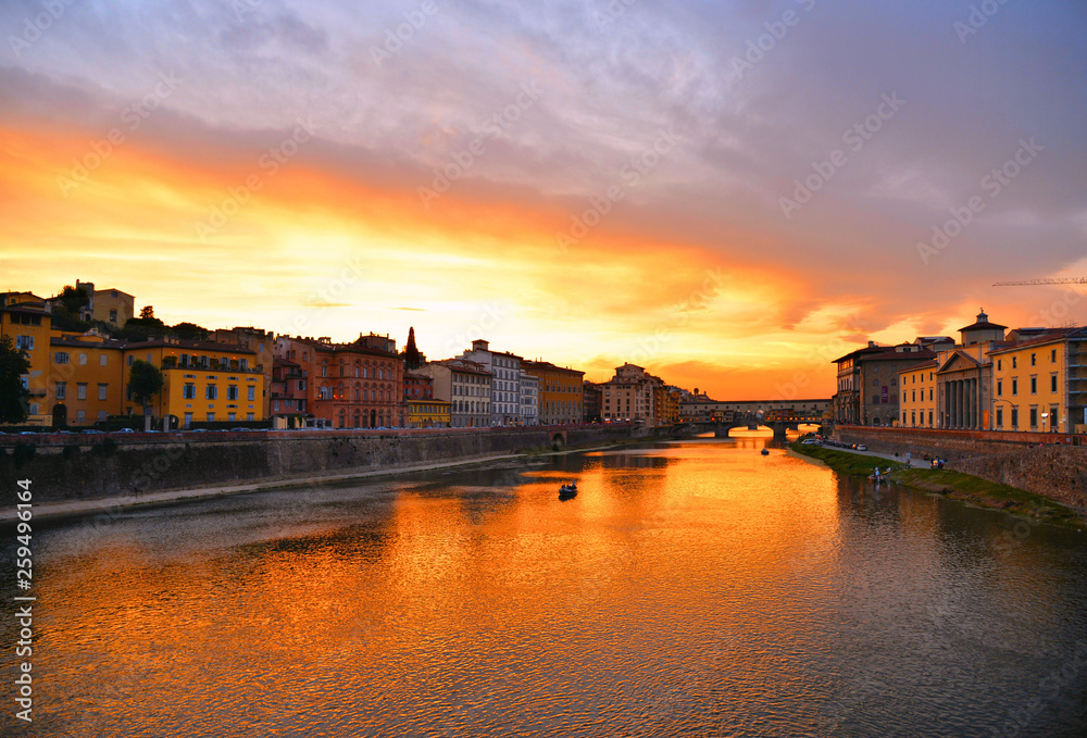 colorful buildings, bridge Ponte Vecchio and water reflections in warm sunset on river Arno with small boats in florence, italy