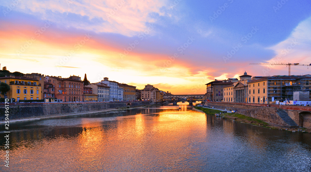 colorful buildings, bridge Ponte Vecchio and water reflections in warm sunset on river Arno with small boats in florence, italy