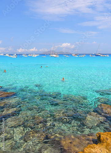 people inside paradise clear torquoise blue water with boats and cloudy blue sky in background in Favignana island, Cala Rossa Beach, Sicily South Italy. © poludziber