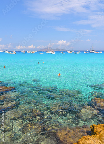 people inside paradise clear torquoise blue water with boats and cloudy blue sky in background in Favignana island, Cala Rossa Beach, Sicily South Italy.