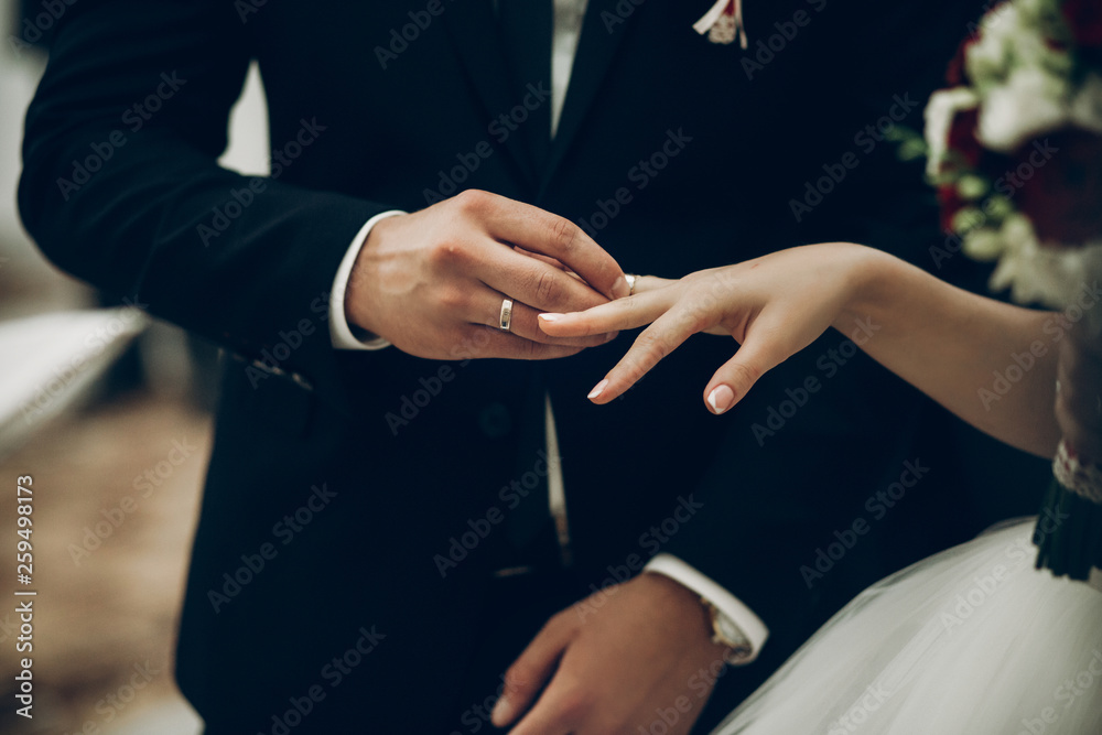 Fototapeta premium bride and groom exchanging wedding rings, putting on fingers during wedding ceremony in church. wedding couple