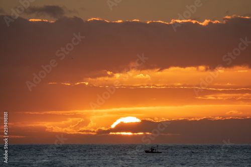 Sun over the ocean skyline with small fishing boat