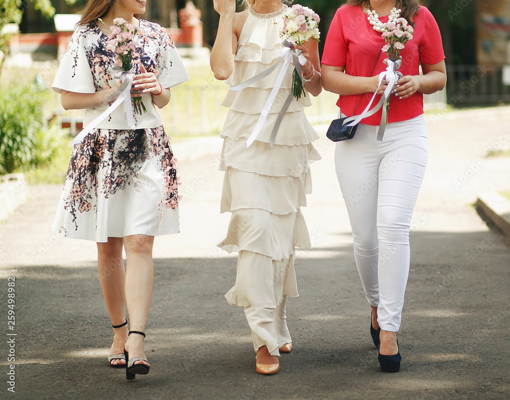 Obraz premium bride in vintage dress and bridesmaids with bouquets walking in sunny park at wedding reception