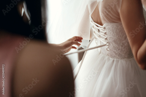 bridesmaids helping bride getting dressed in wedding gown, getting ready and preparation in morning for wedding ceremony.