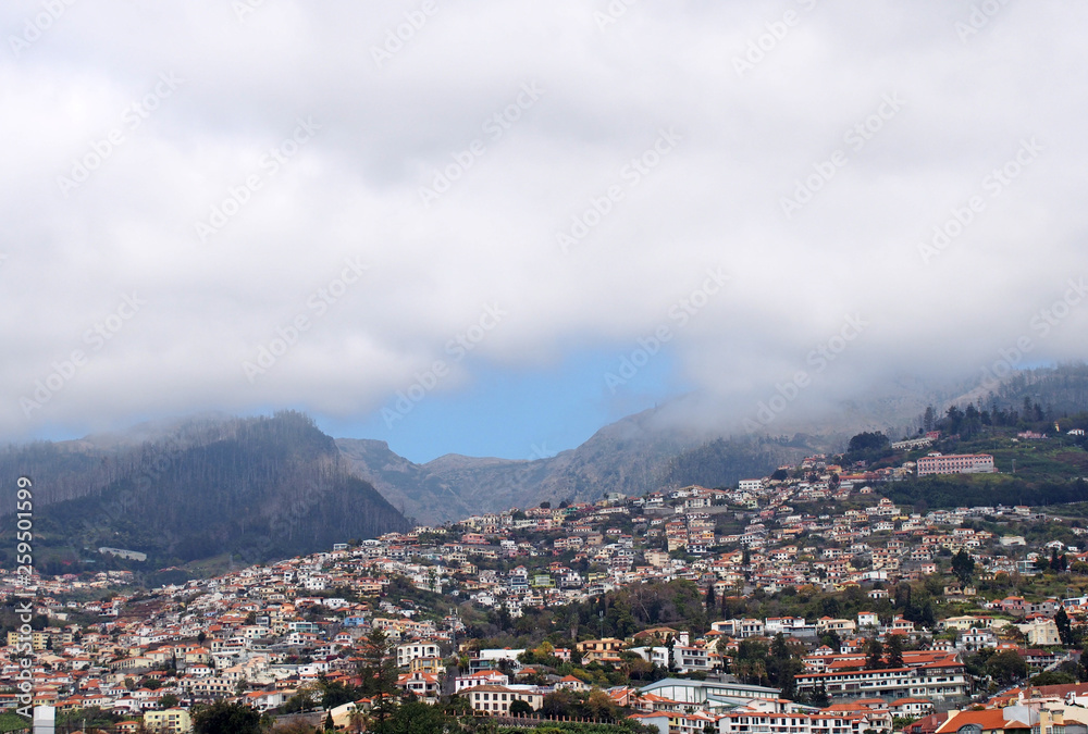 a wide panoramic view of the city of funchal in madeira with houses and tree covered hills under a cloudy sky