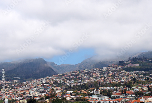 a wide panoramic view of the city of funchal in madeira with houses and tree covered hills under a cloudy sky