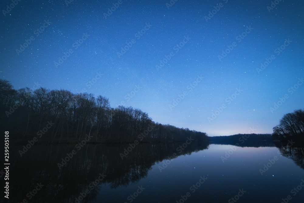 Windless starry night at the forest lake. Star reflections in the water surface Windless starry night at the forest lake. Star reflections in the water surface