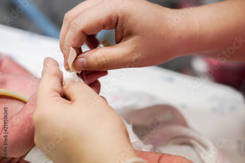 Nurse hands using medical adhesive plaster stick and wrap safely on IV Catheter and sick newborn baby s hand for prepare fill the saline solution and medicine.