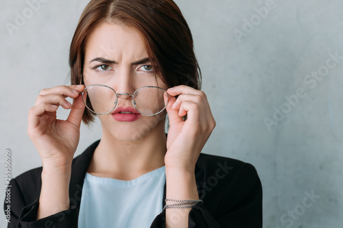 Fotografie Closeup of young business lady looking confused, taking off glasses