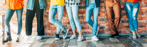 Millennials community. Cropped shot of young people in casual outfits standing against brick wall, socializing during break. photo