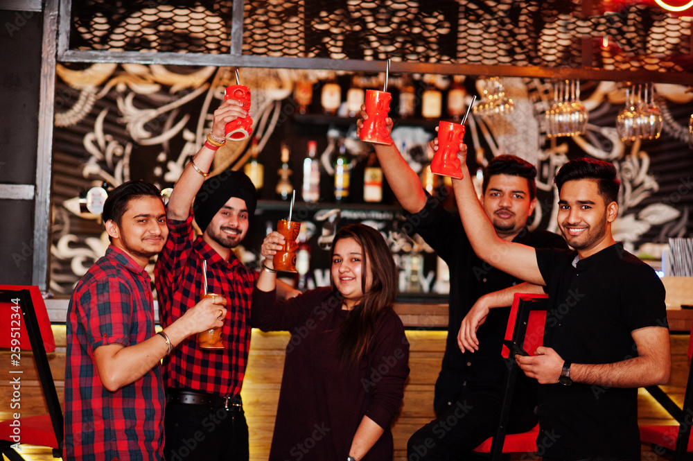  Group of indian friends having fun and rest at night club, drinking cocktails, clinking and cheers near bar counter.