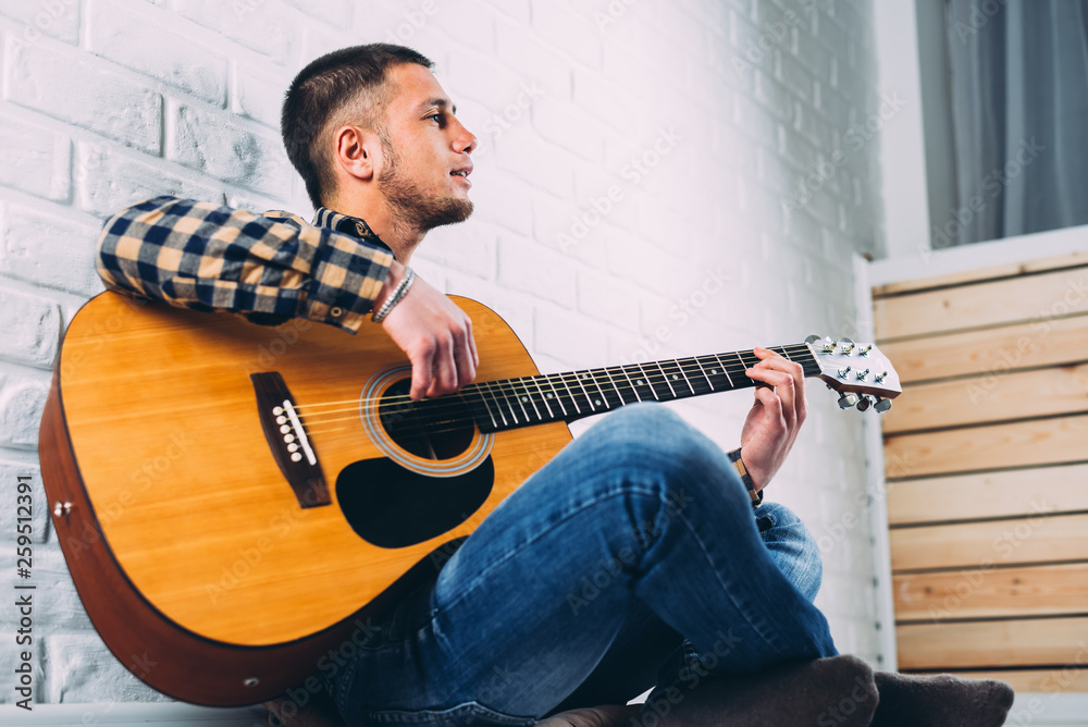 Obraz premium Handsome mature man in casual clothes is smiling while playing guitar at home