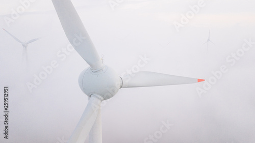 Windmills in the fog at sunrise. Wind turbine from aerial view. Sustainable development, environment friendly.