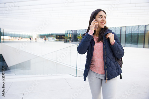 Smiling pretty girl with satchel using mobile phone outdoors