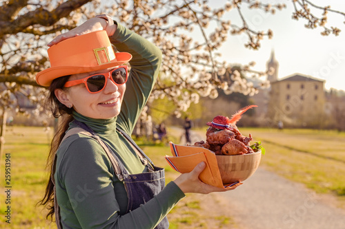 Girl with accessories for the holiday King's Day in the Netherlands, holding a bowl with donuts. Traditional pastries for the festival. Family picnic in the park in spring. Flowering trees 