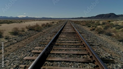 Fast, low aerial view, moving forward along straight railroad tracks in the desert