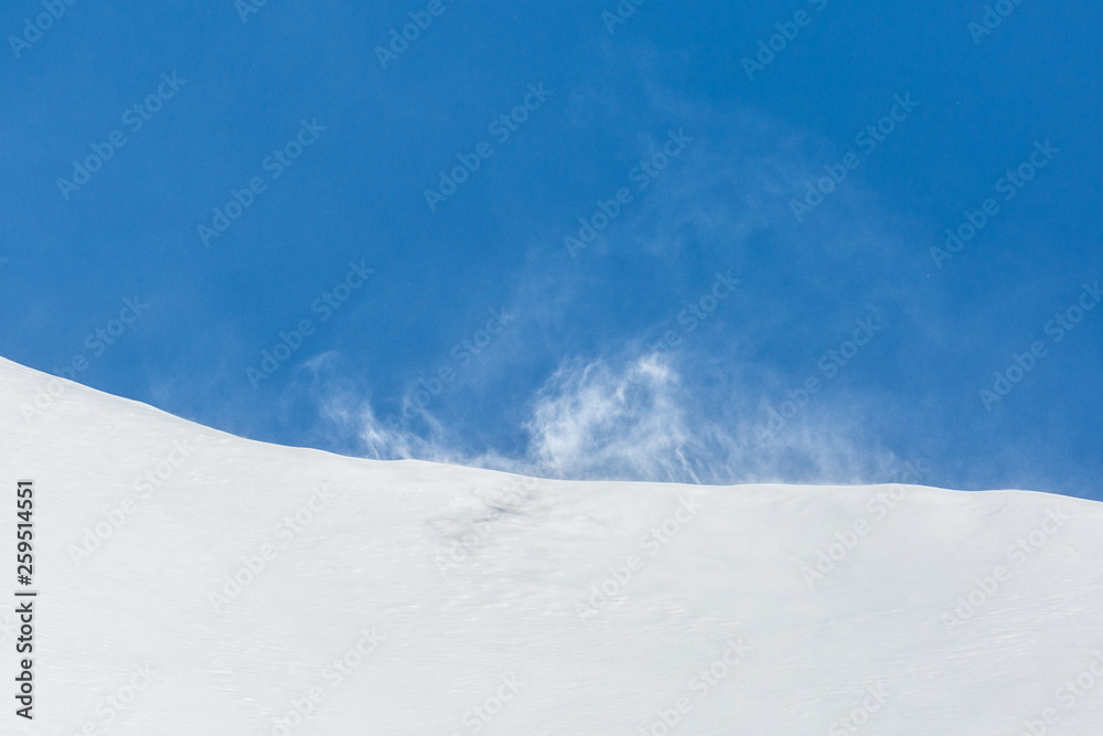 strong gust of wind raising snow, blue sky