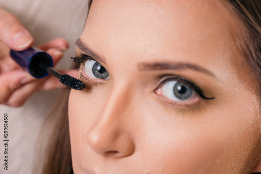 Make up artist applying mascara on female client's eyelashes