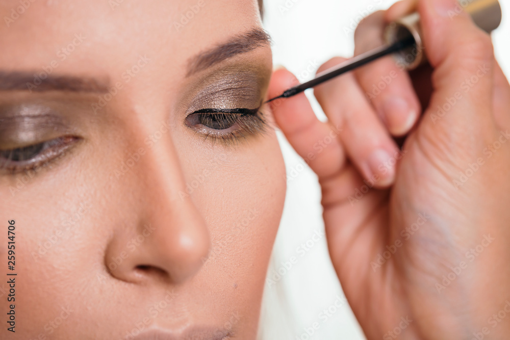 Make up artist applying eyeliner on female client's eyelids