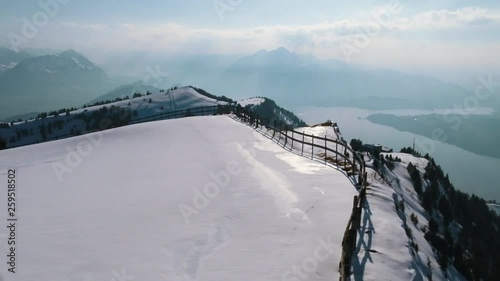 A drone movie over a mountain cliff with a stuning scenic view to a lake.
A fence is visible on the edge of the cliff. A fantastic movie on a winterday in the mountains. photo