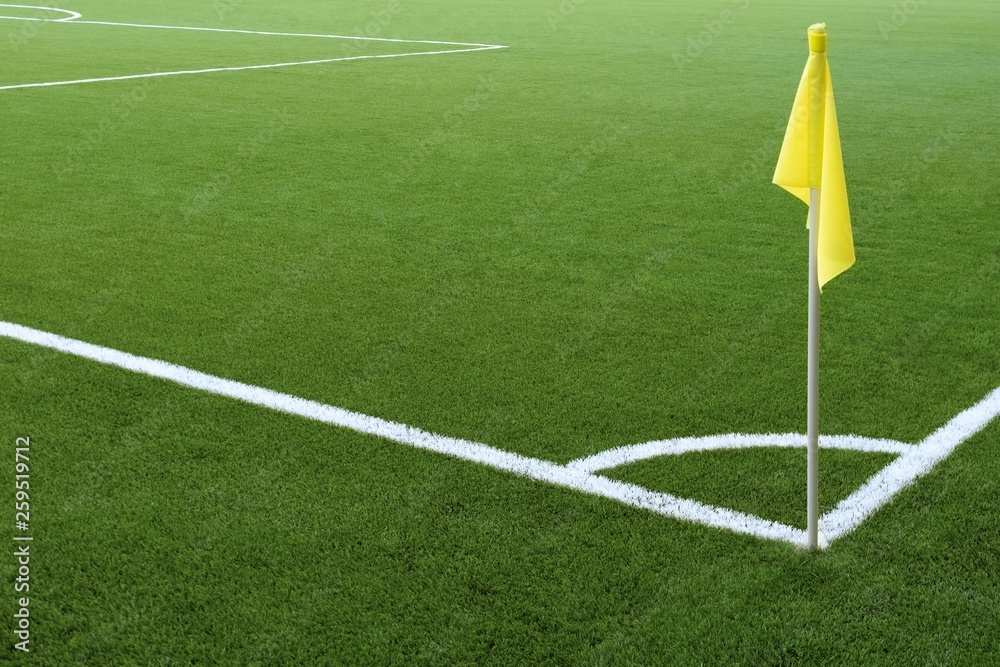 Fototapeta premium Corner of a football field. White markings on green grass and yellow flag. No people and players. Sports concept.
