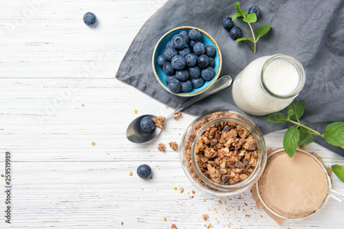 Granola muesli, milk and ripe blueberries with mint leaves, healthy breakfast concept, wooden background, top view