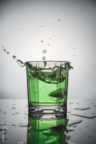 splash of green water in glass on grey background