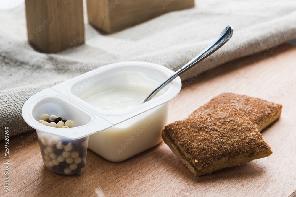 Yogurt with chocolate balls. Double plastic cup with white yogurt and sweet cinnamon cookies.
