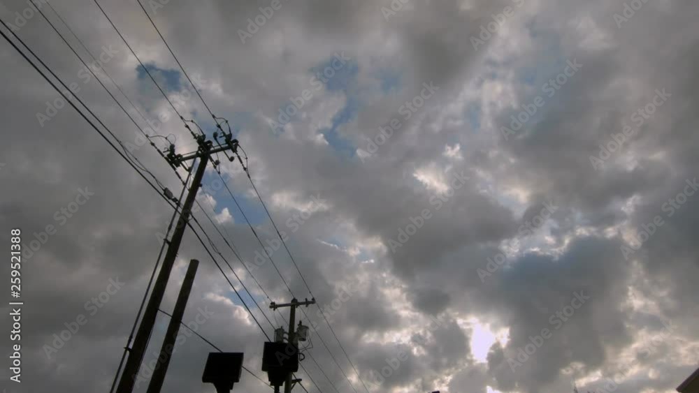 Cloud covered blue sky with sun peeking through and telephone poles in foreground