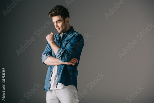 handsome man in denim shirt and jeans looking away on grey background