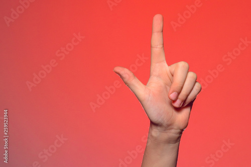 Human hand with folded fingers, shows an index finger that symbolizes a pistol, isolated on a red background