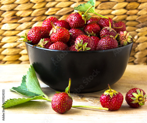 red organic strawberries in a black bowl against the straw wood background .