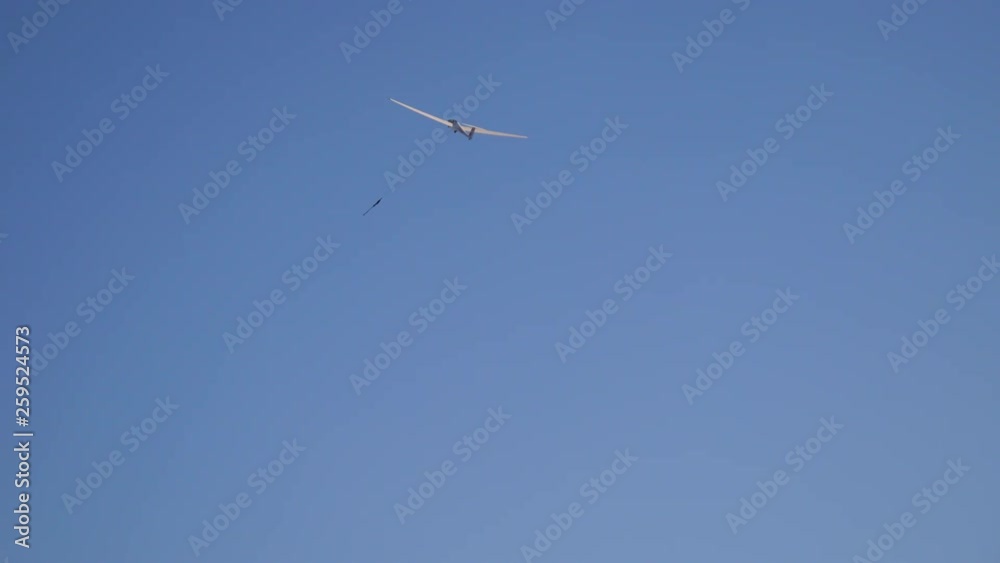 View from below at starting, ascending glider on a wire moving from right to left under blue sky . View from below at starting, ascending glider on a wire moving from right to left under blue sky .
