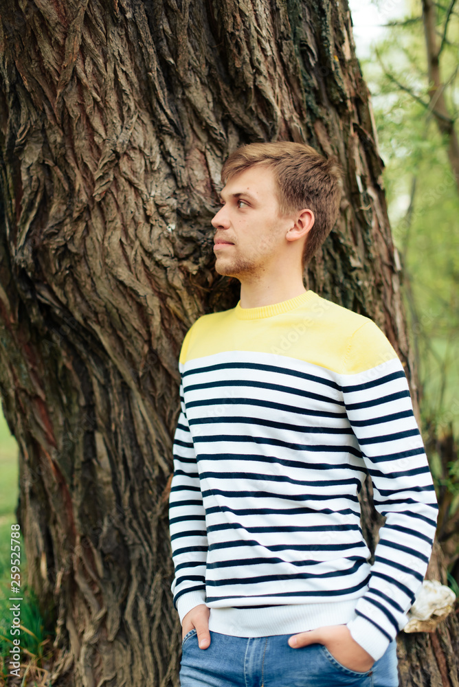 Fototapeta premium a man stands near a tree in a yellow striped jacket in nature 1