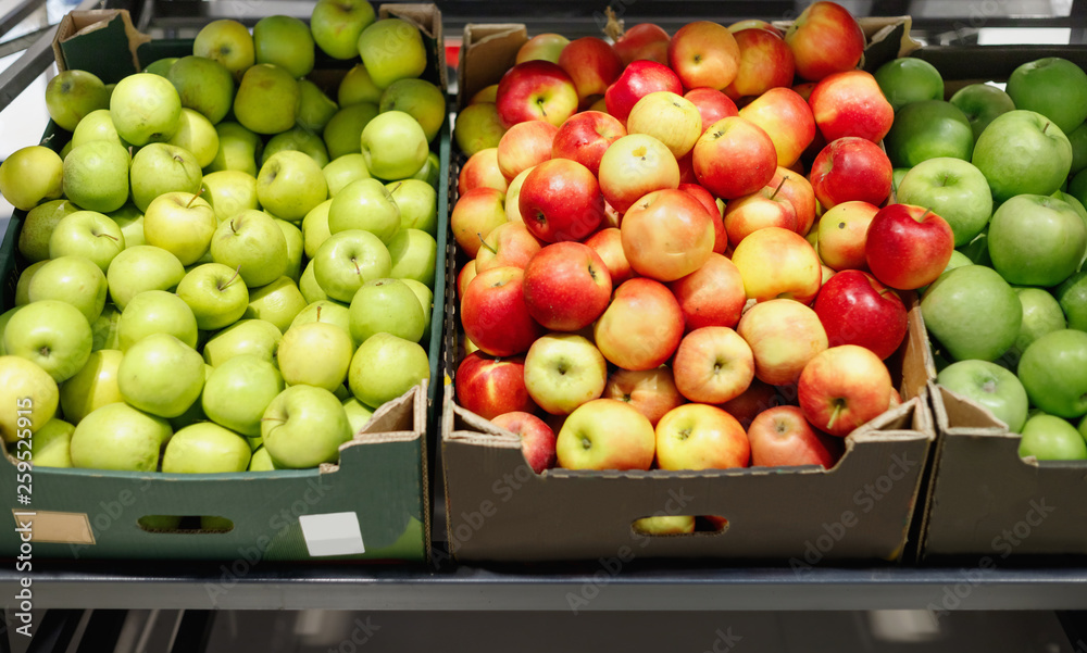 Boxes with ripe red and green apples on shelves of supermarket