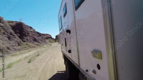 Low side view on an overland RV driving off road through a canyon in the desert.