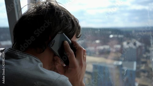 Slowmotion. Close-up of a man near a window on a sunny morning who speaks by mobile phone