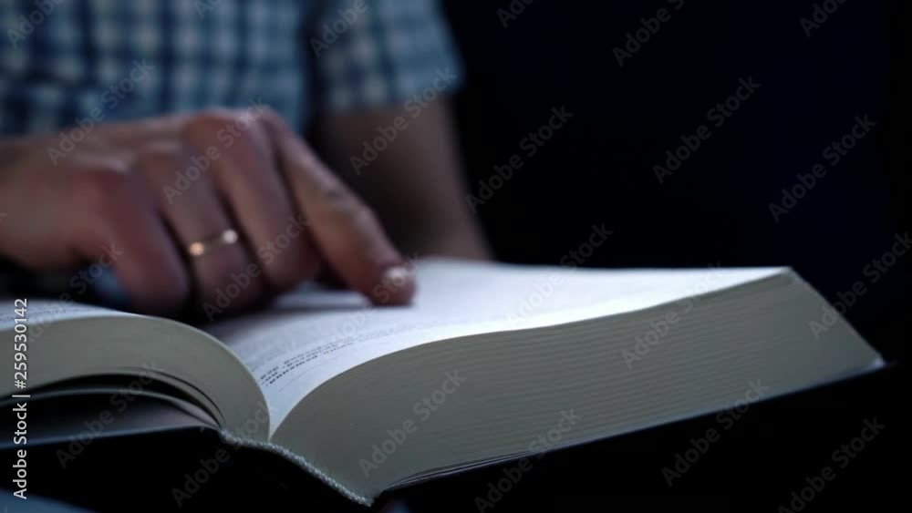 Slowmotion. A man runs his finger through the pages of a thick book in search of necessary information while sitting at home on the couch Slowmotion. A man runs his finger through the pages of a thick book in search of necessary information while sitting at home on the couch