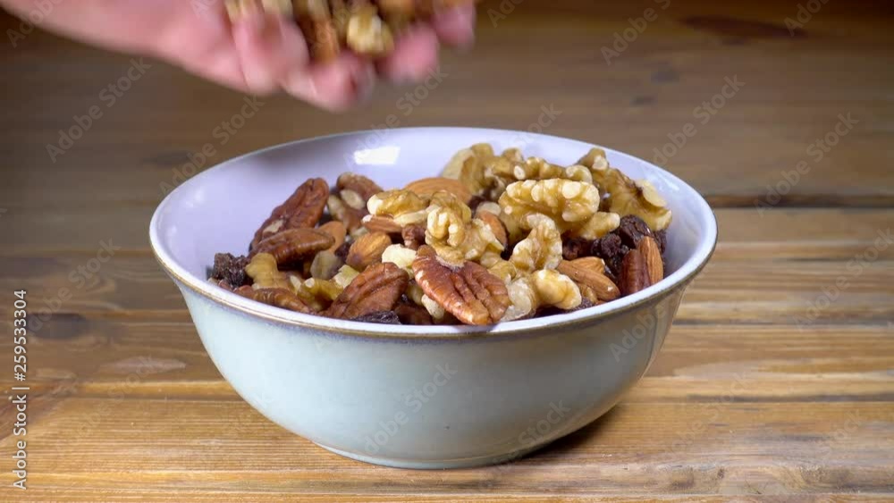 Two female hands dipping into a healthy snack of mixed nuts and raisins, in a ceramic bowl on a pine worktop. Two female hands dipping into a healthy snack of mixed nuts and raisins, in a ceramic bowl on a pine worktop.