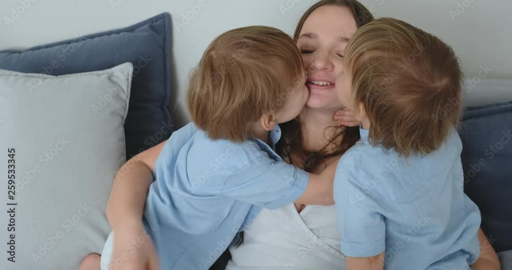 Mom is sitting on the couch with a laptop. Two boys children sing and kiss their mom Mom is sitting on the couch with a laptop. Two boys children sing and kiss their mom