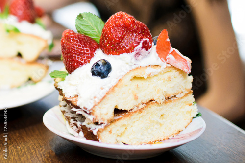 A piece of cake with strawberries in cream  blueberries and mint leaves  on a plate  in light colors close-up