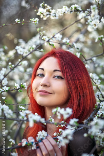 The girl with red hair inhales the fragrance of the flowers of the tree. Outdoor. Spring.