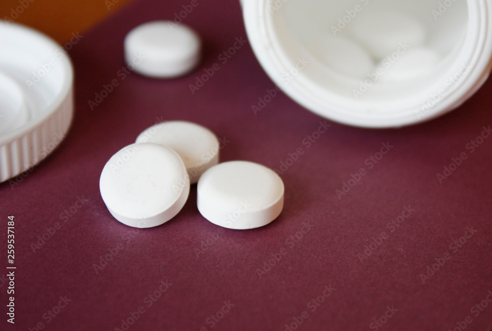 white capsules poured out of the container, red, burgundy background, close-up