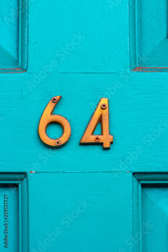 House number 64 with the sixty-four in bronze metal on the middle cross of the wooden panel on the turquoise wooden house door