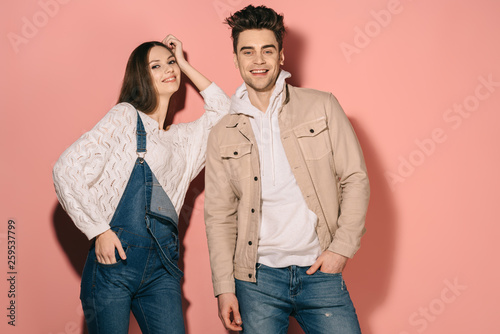 brunette and beautiful girlfriend in denim overalls and handsome boyfriend smiling and looking at camera